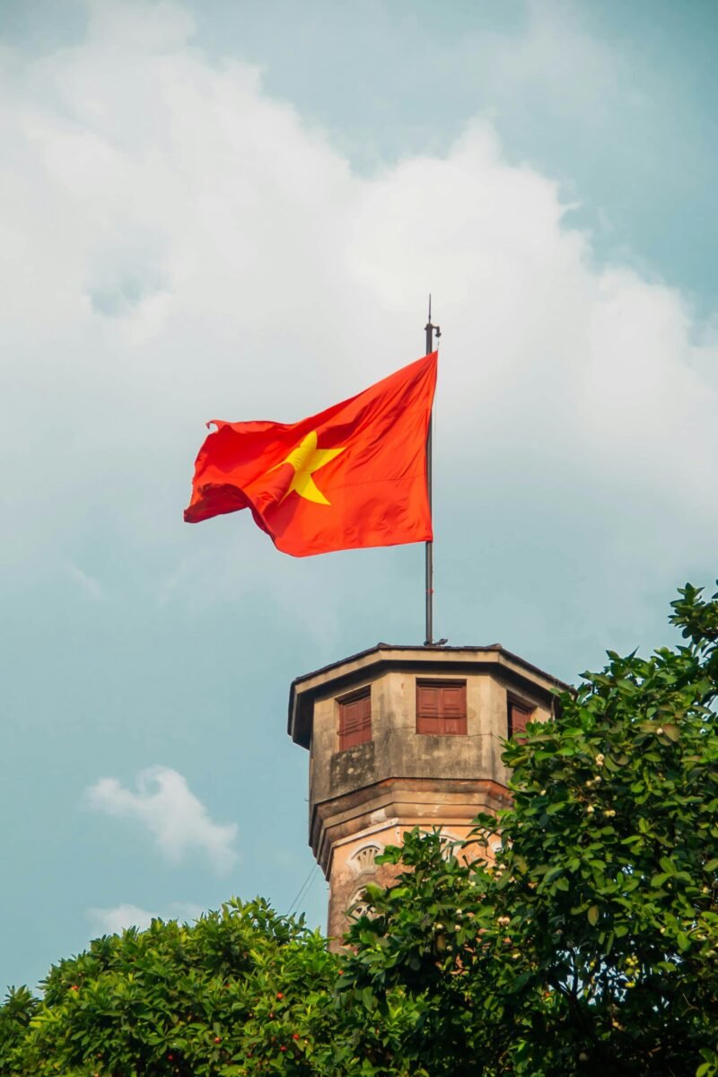 Vietnamese national flag waving on Hanoi Flag Tower under a clear blue sky.