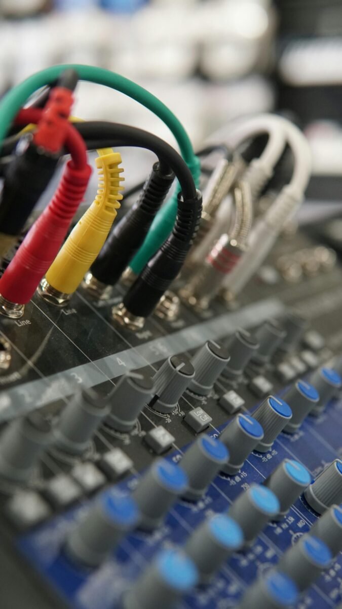 Detailed view of audio mixer controls and colorful connecting cords in a studio environment.